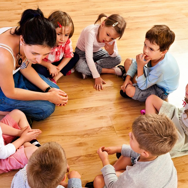Nursery School / Izabela Habur, izusek Nursery school children sitting in circle on the floor in a playroom and listening to their teacher. High angle view.